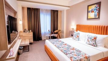 Ein Hotelzimmer mit einem großen Bett, einem Schreibtisch, einem Sessel, einem kleinen Tisch und einem Fernseher.