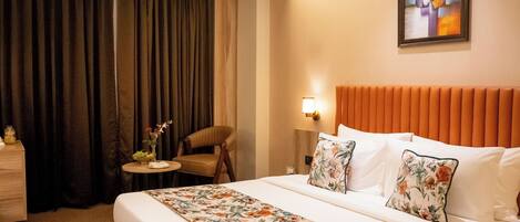 A hotel room with a large bed, a chair, a small table with a vase of flowers, and a painting on the wall.