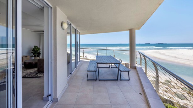 A balcony with a table and benches overlooking a beach.