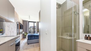Una habitación de hotel moderna con una cama grande, zona de ducha y kitchenette.