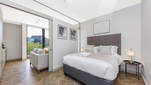 A modern bedroom with a large bed, a gray headboard, and a view of the city through a large window.