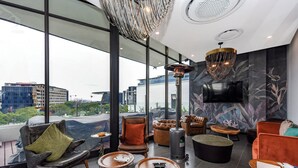 A modern lounge with leather chairs, a fireplace, and large windows offering city views.