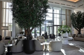 Un hall d’entrée moderne, agrémenté d’un grand arbre, de sièges confortables et de grandes fenêtres.