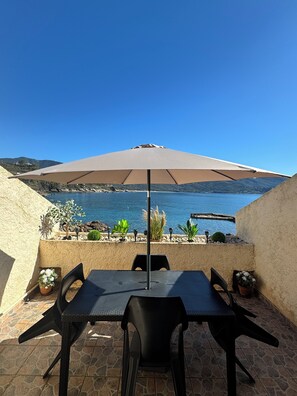 A patio with a table and chairs, a large umbrella, and a view of the sea.