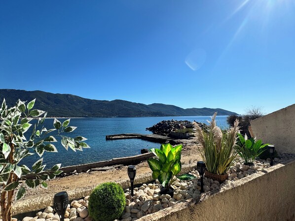 A coastal landscape with a rocky shoreline, a small structure, and various plants.