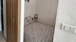 Une chambre avec une porte coulissante en bois, un lit avec une literie à motifs floraux, une petite table de chevet et un luminaire fixé au mur.