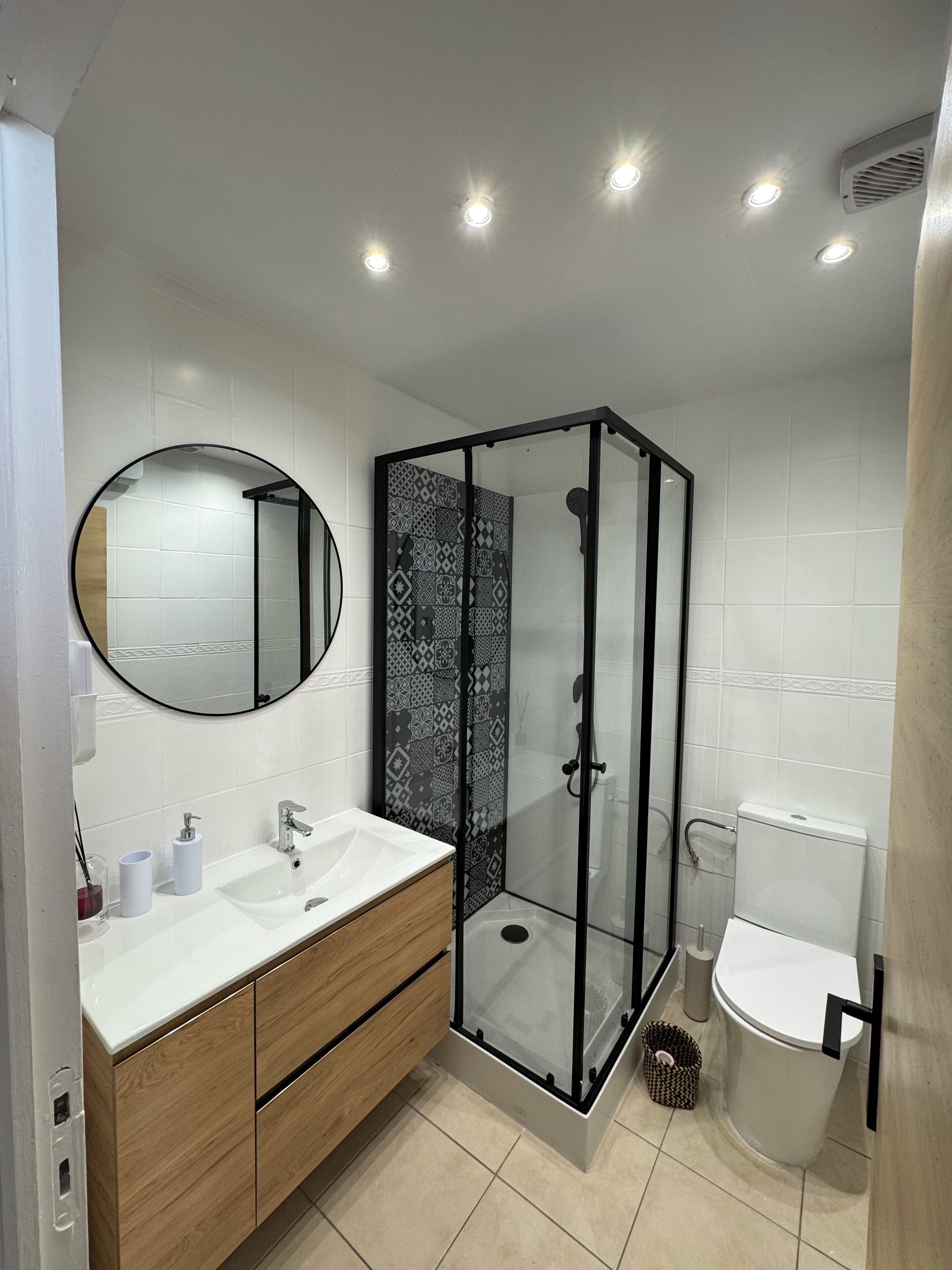 Une salle de bain moderne avec une douche à parois de verre, un miroir rond, un lavabo blanc et des toilettes.
