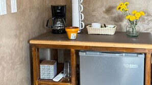 Eine Küchenzeile mit Kaffeemaschine, gestapelten Tassen, einem kleinen Kühlschrank und einer Vase mit Blumen.