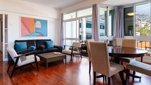 A spacious living area with a sofa, chairs, a coffee table, and a dining table. Large windows provide a view of the cityscape. - GuestReady - Wake Up to the Heartbeat of Madeira (Funchal)