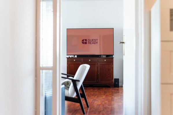 A hotel room with a wooden cabinet, a television displaying "GUEST READY", and a chair.