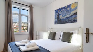 A hotel room with a bed, a painting, a window with a view, and a door. - GuestReady - Wake Up to the Heartbeat of Madeira (Funchal)