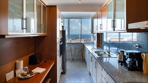 A modern kitchen with a view of the sea, featuring stainless steel appliances, wooden cabinets, and a granite countertop. - GuestReady - Wake Up to the Heartbeat of Madeira (Funchal)