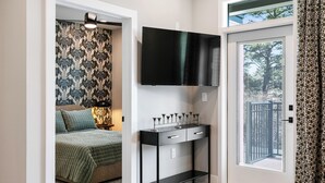 A bedroom with a bed, a bedside table with a lamp, a TV mounted on the wall, and a door leading to a balcony.
