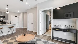 A modern kitchen with a microwave, stove, and bar stools. There is a dining area with a round table and a black console table with drawers.