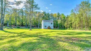 A white house with a front porch, surrounded by a grassy yard and tall trees.