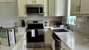 A modern kitchen with white cabinets, a stainless steel microwave, oven, and dishwasher. There is a wooden countertop, a sink, and a window with a view.