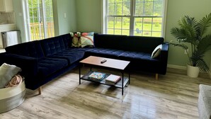 A living room with a dark blue sectional sofa, a coffee table, and a large window with a view of greenery.