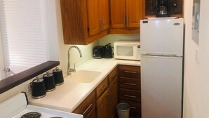 Una cocina compacta con armarios de madera, un refrigerador blanco, un microondas, un tostador y una estufa.