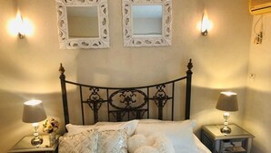 Una cama bien hecha con sábanas blancas y almohadones decorativos, flanqueada por dos mesitas de noche con lámparas y un pequeño florero.