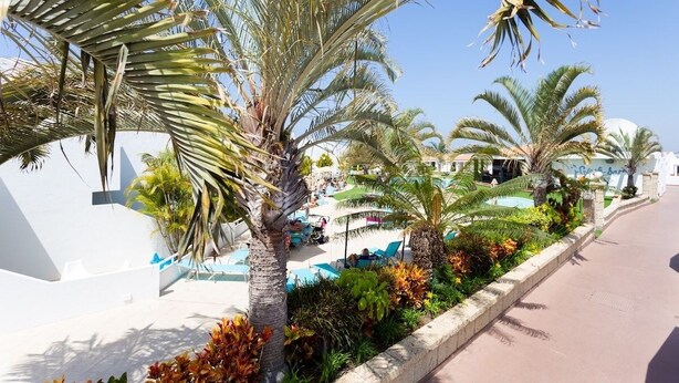 Un resort con palmeras, una zona de piscina y un edificio blanco con un letrero.