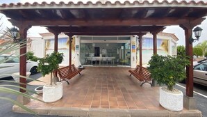 Un espacio al aire libre cubierto con bancos, plantas en macetas y la entrada de un edificio.