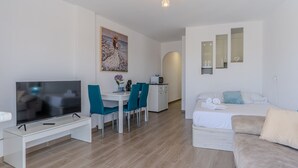 Una habitación moderna, bien iluminada, con televisión, comedor, kitchenette y una cama.