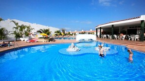 Piscina con fuente de agua, sillas de descanso y sombrillas.