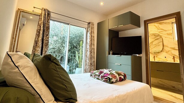 A modern bedroom with a large bed, a flat-screen TV, a wardrobe, and a bathroom with a marble vanity.