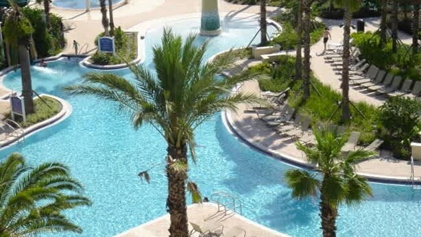 A resort pool area with multiple swimming pools, palm trees, and lounge chairs. - No Stairs 2BR Apartment at Champions Gate (Davenport)