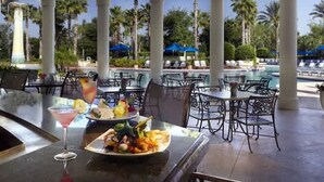 An outdoor dining area with tables and chairs, a pool in the background, and palm trees. - No Stairs 2BR Apartment at Champions Gate (Davenport)