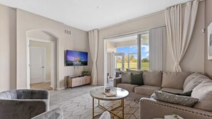 A spacious living room with a sofa, armchairs, a coffee table, and a television. - No Stairs 2BR Apartment at Champions Gate (Davenport)
