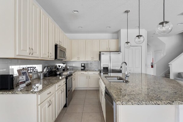 A modern kitchen with white cabinets, granite countertops, stainless steel appliances, and pendant lighting. - Amazing House at Bella Vida 5BR (Kissimmee)