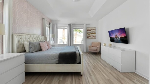 Ein modernes Schlafzimmer mit Bett, Nachttischen, Fernseher und einem Fenster mit Vorhängen.