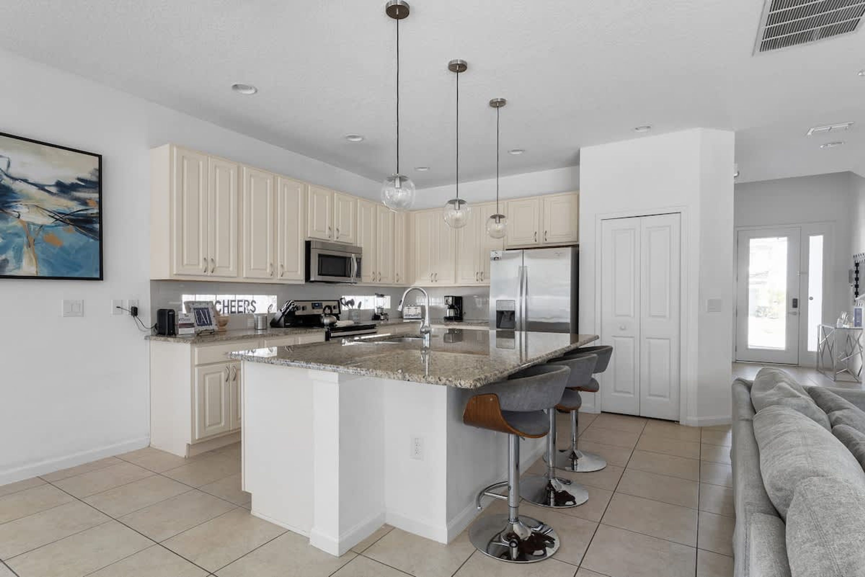 A modern kitchen with white cabinets, a central island with bar stools, stainless steel appliances, and pendant lighting.