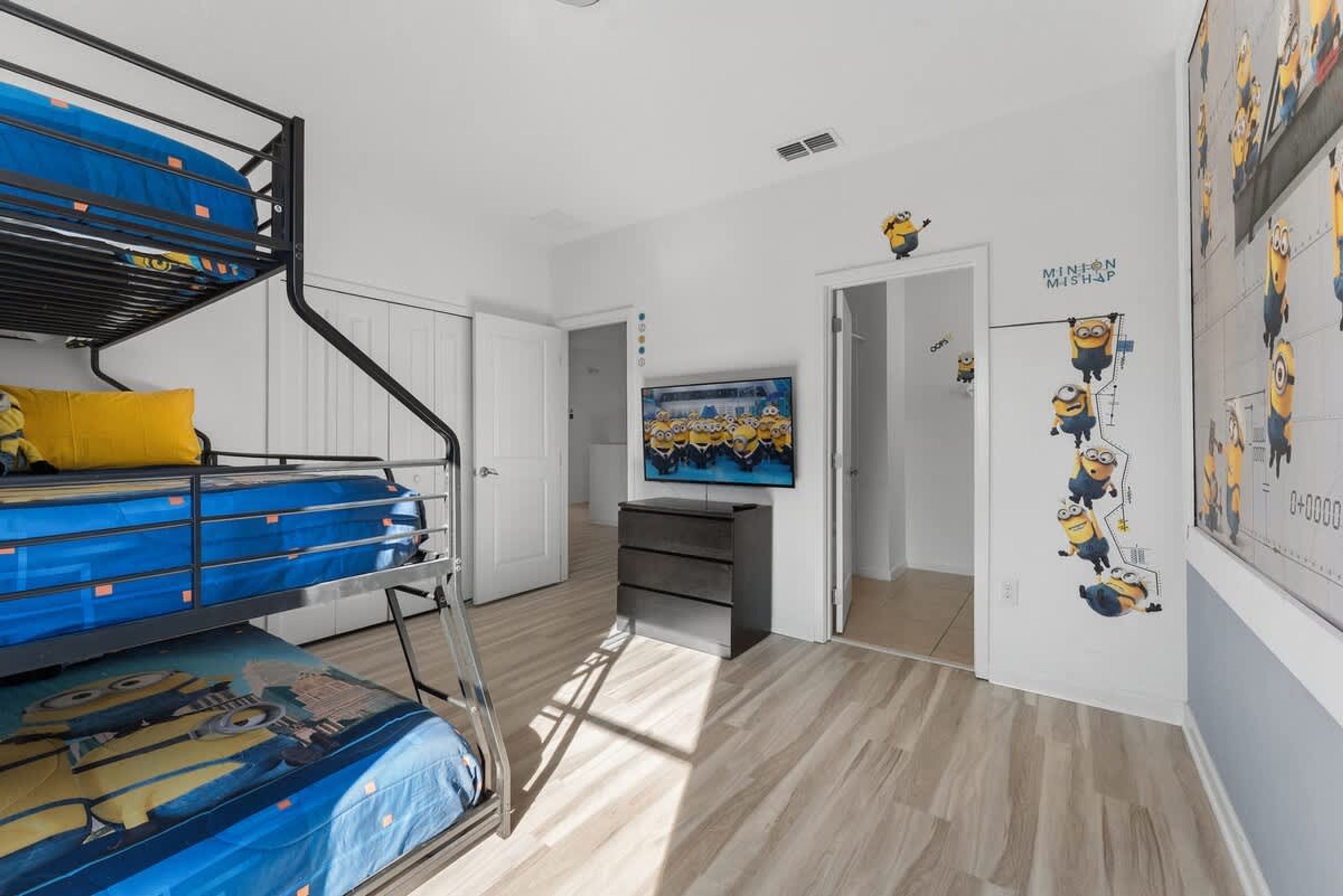 A bunk bed with a blue mattress and a yellow pillow, a television on a stand, and Minion-themed wall decorations.