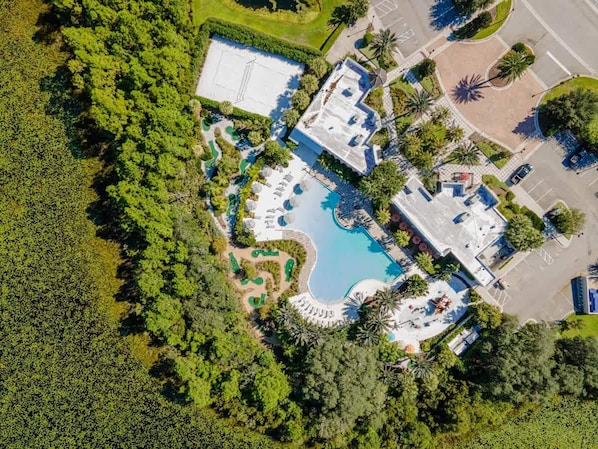 Vista aérea de un complejo turístico con una piscina central, jardines ajardinados y varias edificaciones.