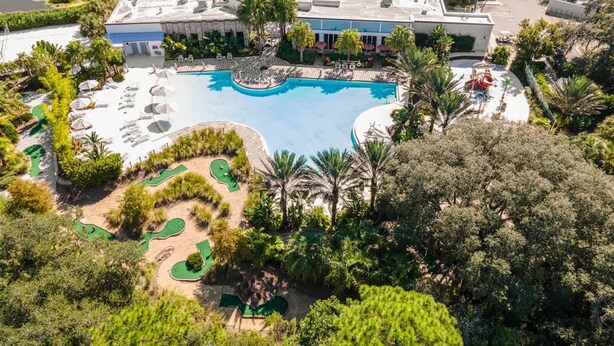 Vista aérea de un complejo turístico con una gran piscina, tumbonas y un campo de golf.