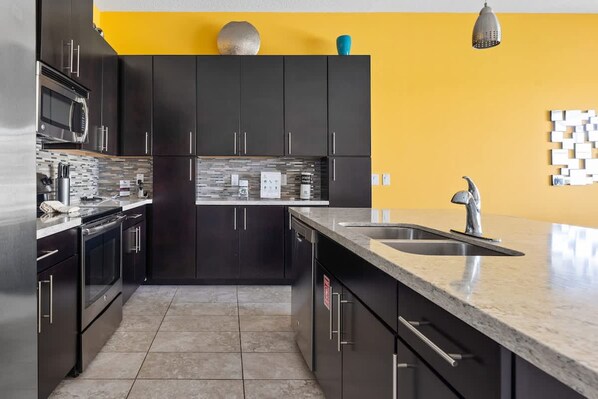 A modern kitchen with dark cabinets, a stainless steel refrigerator, and a yellow accent wall. - Comfortable Vacation Home up to 10 People Ef466 (Davenport)
