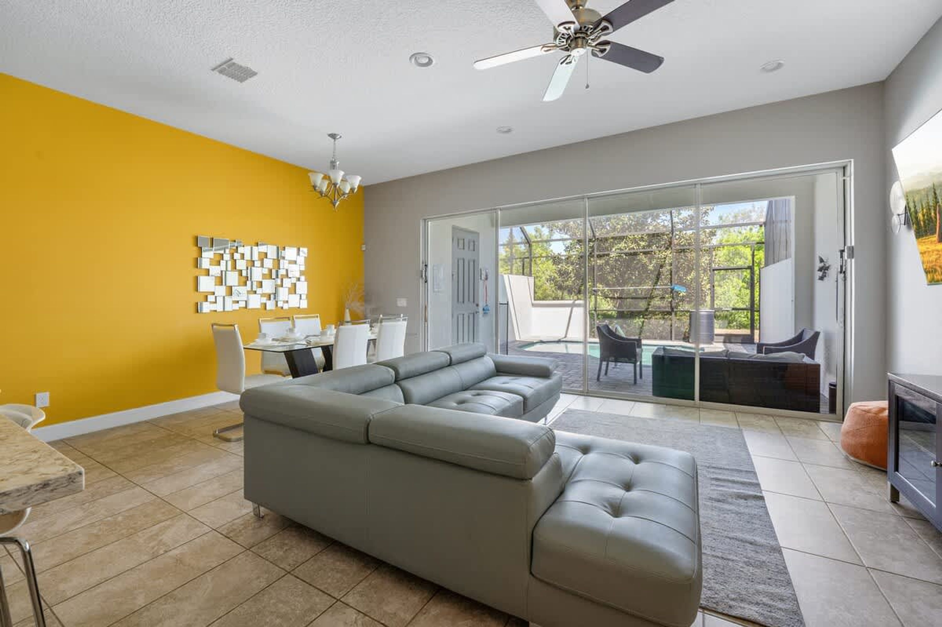 A modern living room with a sectional sofa, a dining area, and a sliding glass door leading to an outdoor patio.