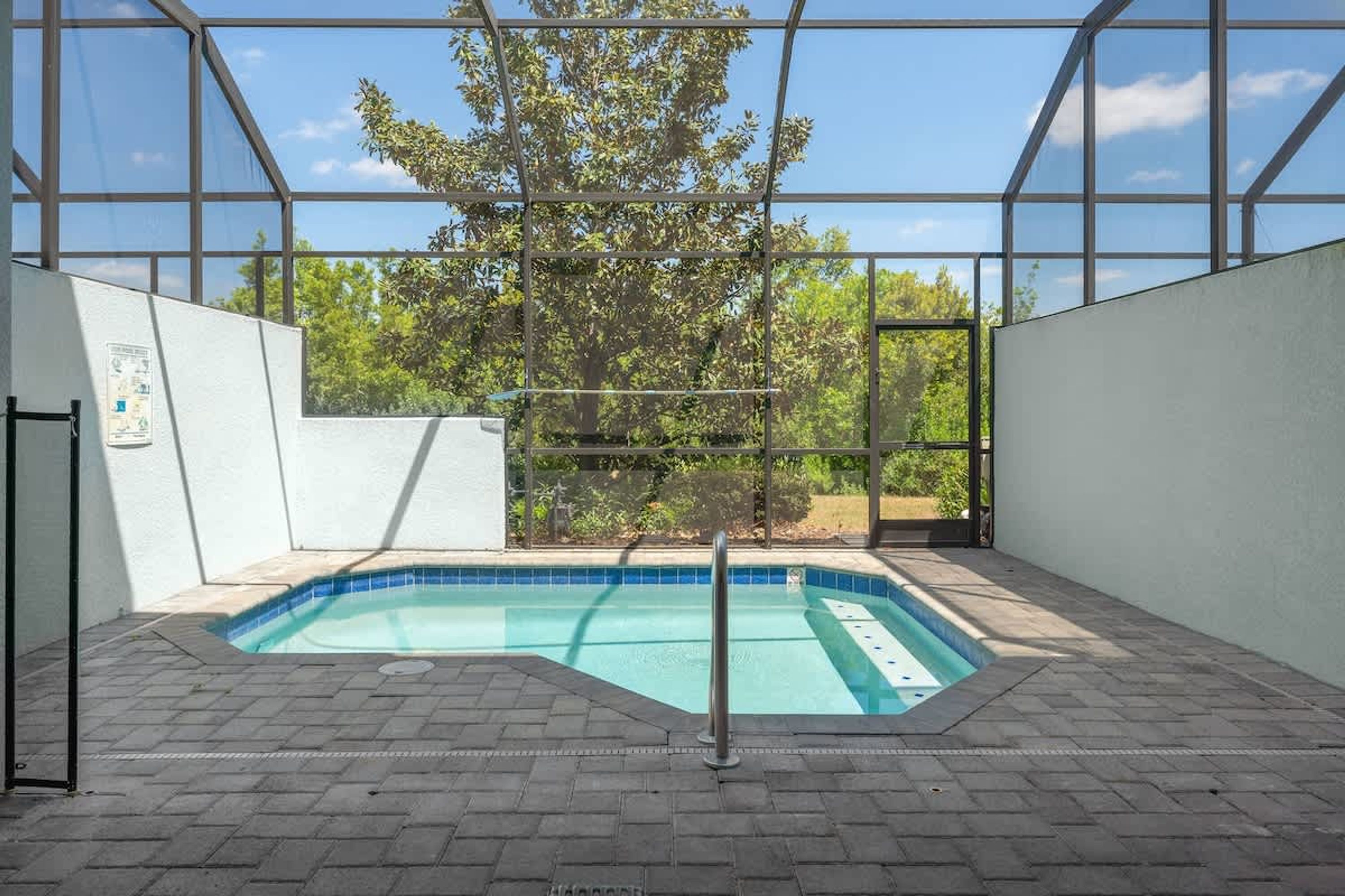 An indoor swimming pool with clear glass walls, a tiled floor, and a view of trees outside.