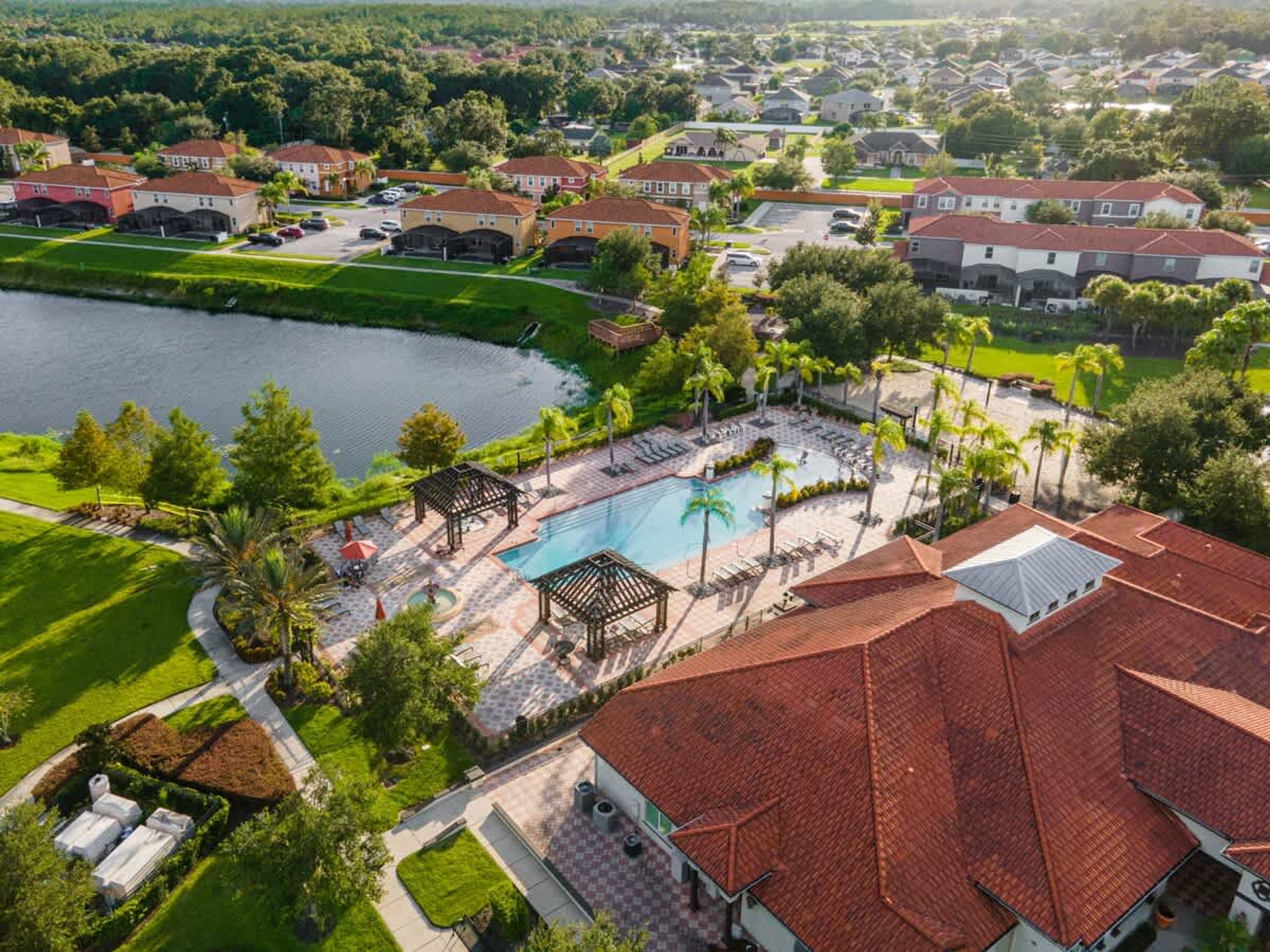 An aerial view of a residential area with a swimming pool, palm trees, and houses.