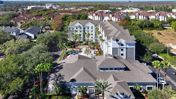 A large hotel with multiple floors, a parking lot, and surrounding greenery. - 1BR Free Shuttle to Disney Parks (Orlando)