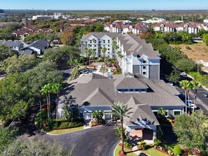 A large hotel with multiple floors, a parking lot, and surrounding greenery. - 1BR Free Shuttle to Disney Parks (Orlando)