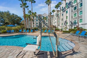 Un espace piscine d’hôtel avec un toboggan, des chaises longues et des palmiers.