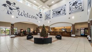 A spacious lobby with a large Christmas tree, a reception desk, and Mickey Mouse decorations on the walls. - 1BR Free Shuttle to Disney Parks (Orlando)