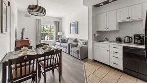 A modern kitchen with white cabinets, a black refrigerator, and a dining area with a wooden table and chairs. - 1BR Free Shuttle to Disney Parks (Orlando)