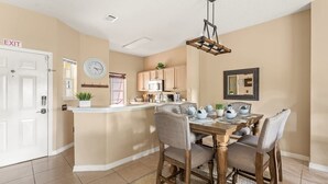A dining area with a wooden table and chairs, a kitchen in the background, and an exit sign on the wall. - Harry Potter Themed 3 BR (Kissimmee)
