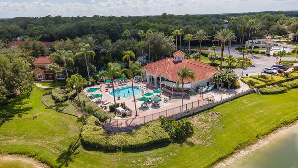 An aerial view of a resort with a swimming pool, palm trees, and a lake. - Harry Potter Themed 3 BR (Kissimmee)