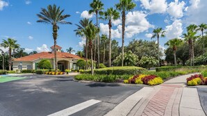 A well-maintained landscaped area with palm trees, a paved walkway, and a building with a red roof. - Harry Potter Themed 3 BR (Kissimmee)