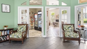 A room with two wooden chairs with floral upholstery, a bookshelf, a refrigerator, and a dining area with a table and chairs. - Harry Potter Themed 3 BR (Kissimmee)